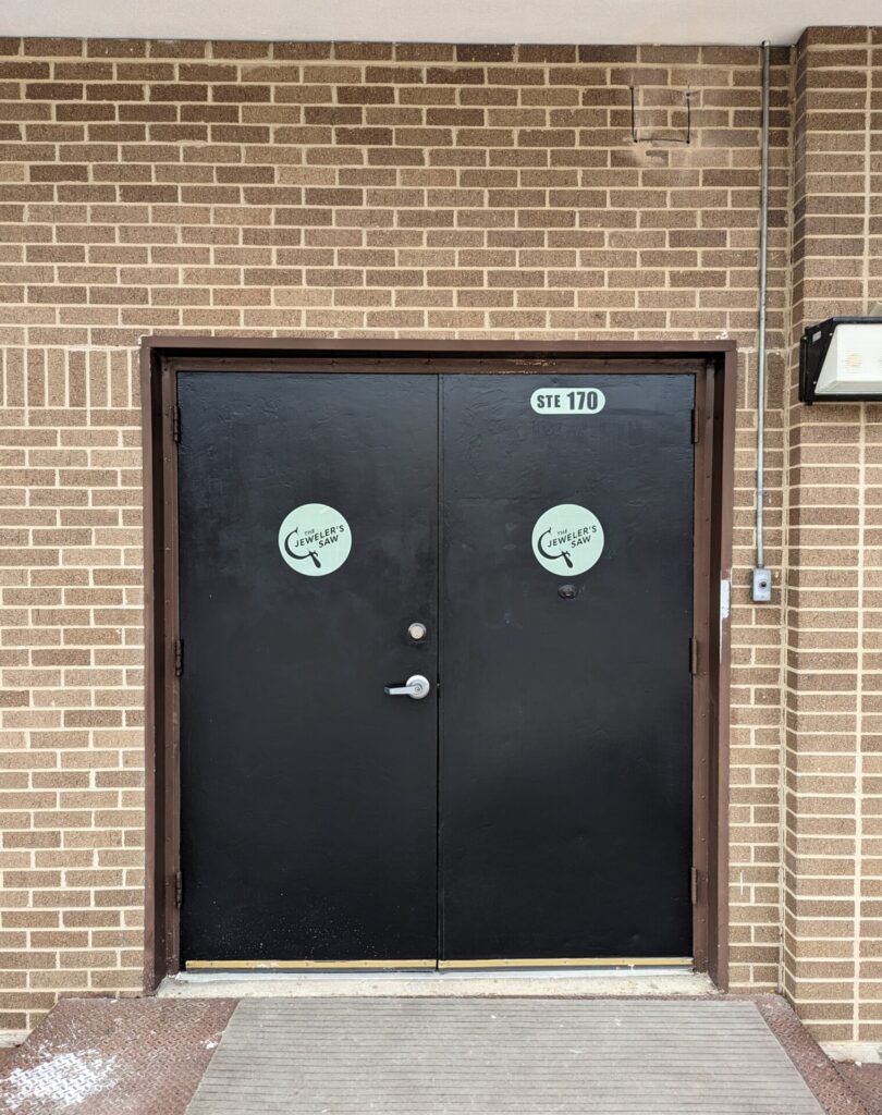 Studio entrance to the Jeweler's Saw studio at Good Dad tudios. Two signs on black doors